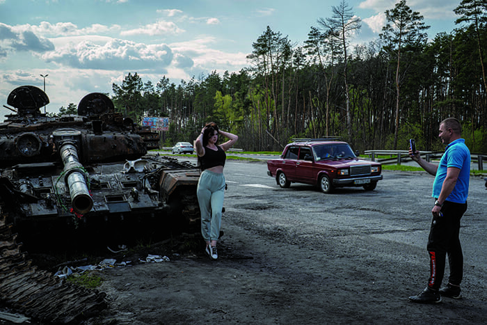 キーウに向かう高速道路でロシアの戦車と撮影する女性。4月の キーウ州奪還後、地元に戻る市民にとってこうした戦車の残骸は 勝利の記念碑になった（ウルフギャング・シュワン撮影、5月2日）
