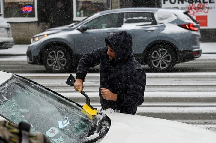 車の雪をかく男性
